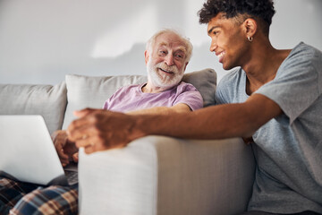 Stock image of older male adult sitting next to younger male representing a caregiver relationship.